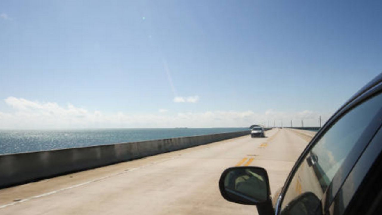 Alt text: View of a city street through a car windshield, showcasing buildings and pedestrians in motion. 
