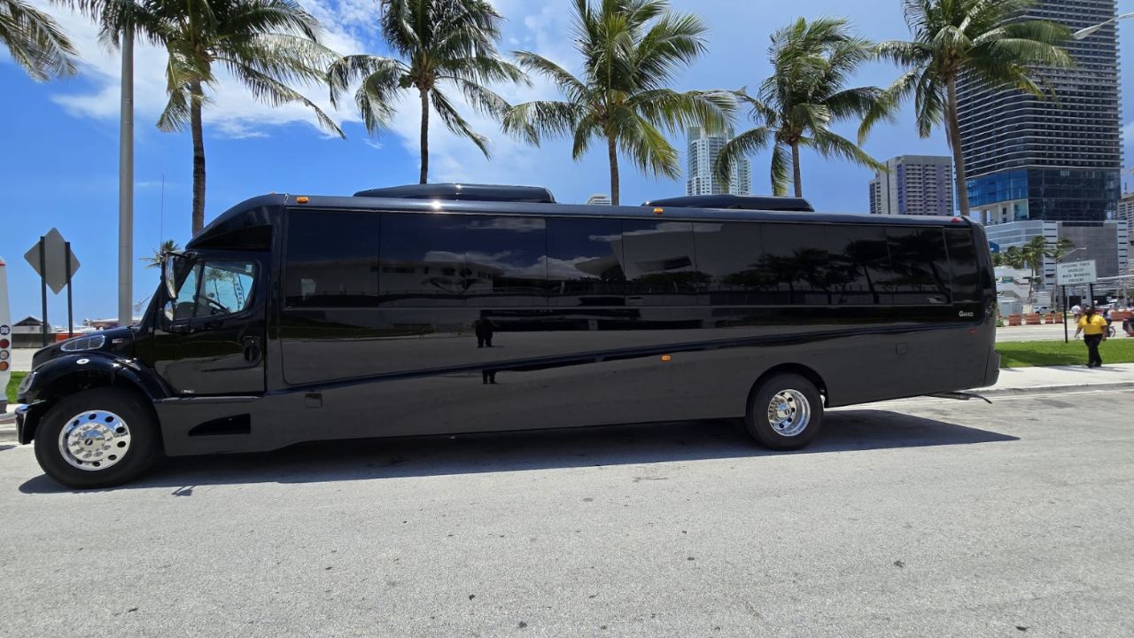 Black luxury motor coach by System Shuttle Miami parked along a palm-lined street 