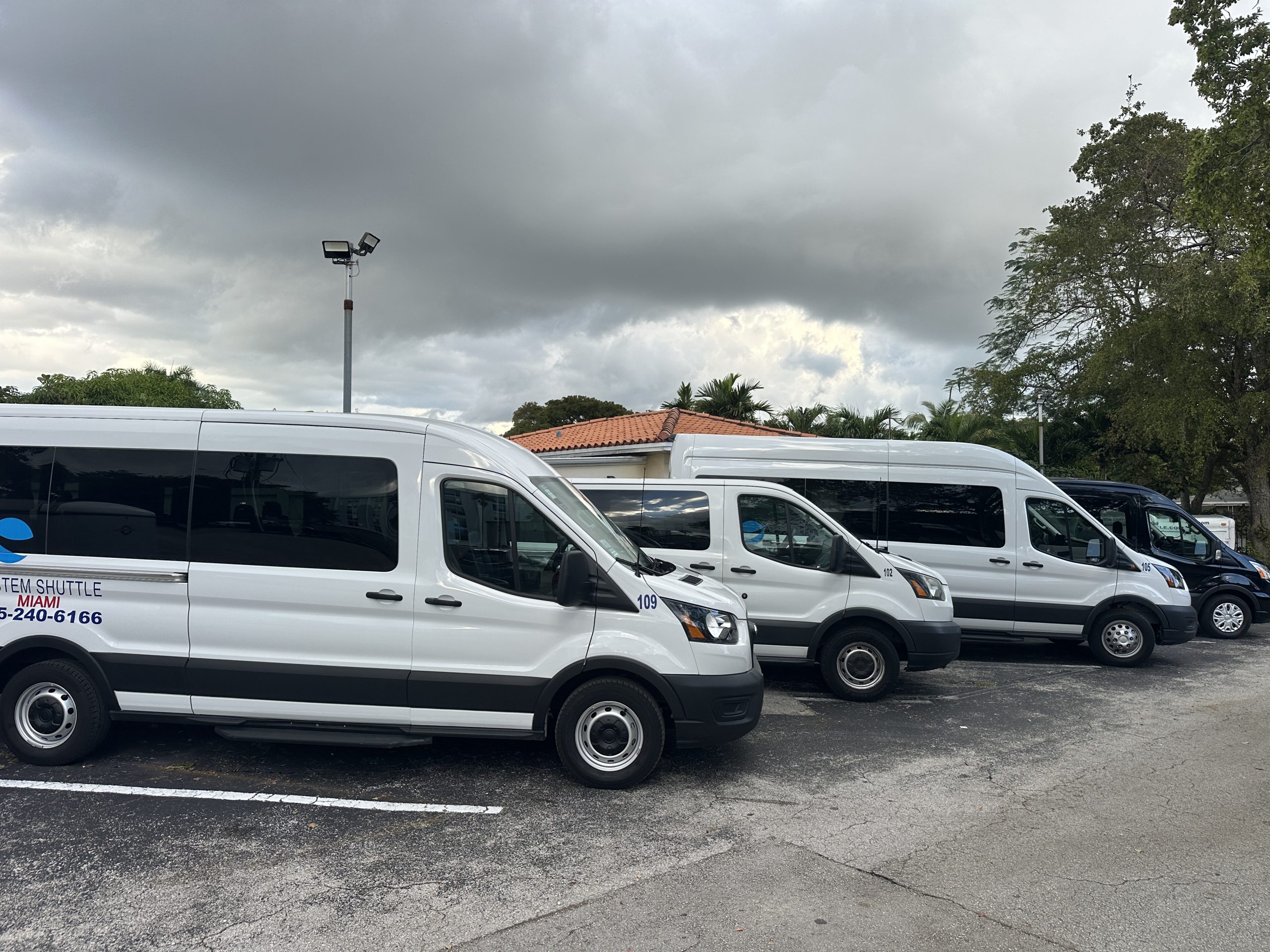Fleet of System Shuttle Miami passenger vans parked in a lot.