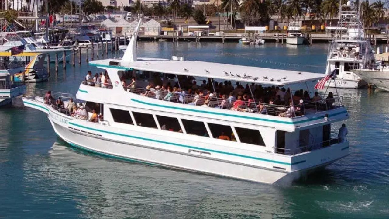 Large white sightseeing boat filled with passengers cruising through a marina 