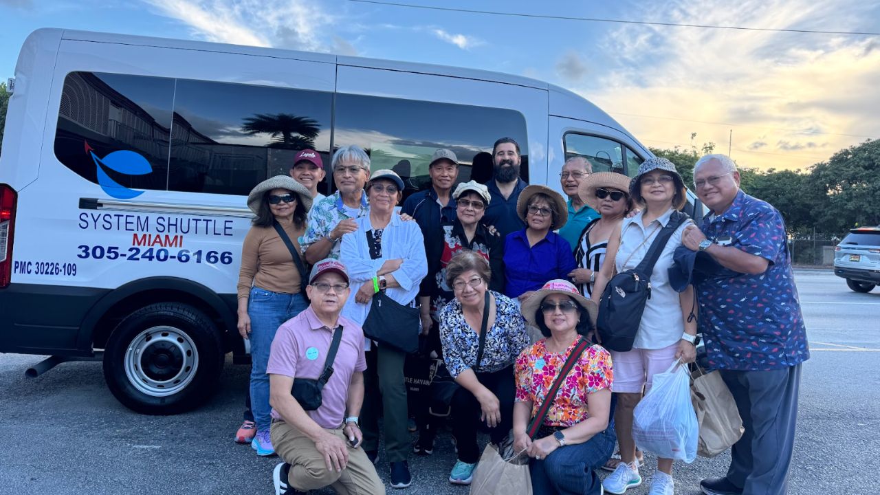 Group of travelers posing in front of a white System Shuttle Miami van