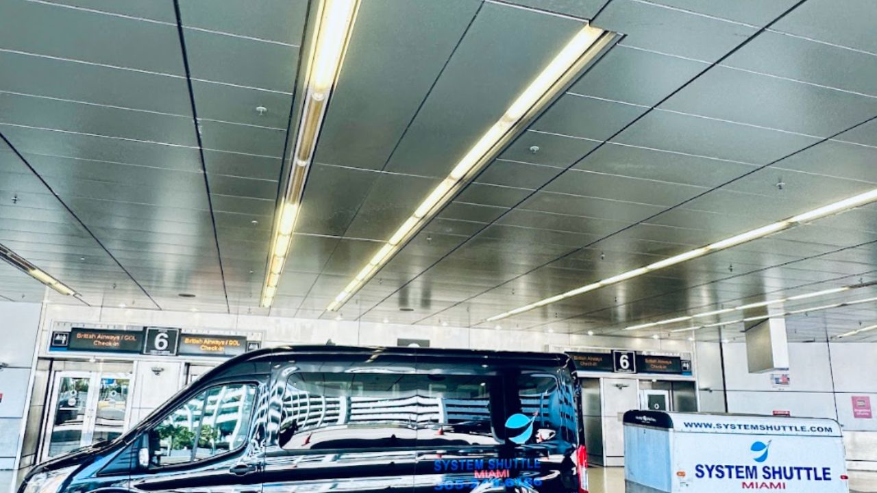 Black System Shuttle Miami van with attached luggage trailer parked outside an airport terminal