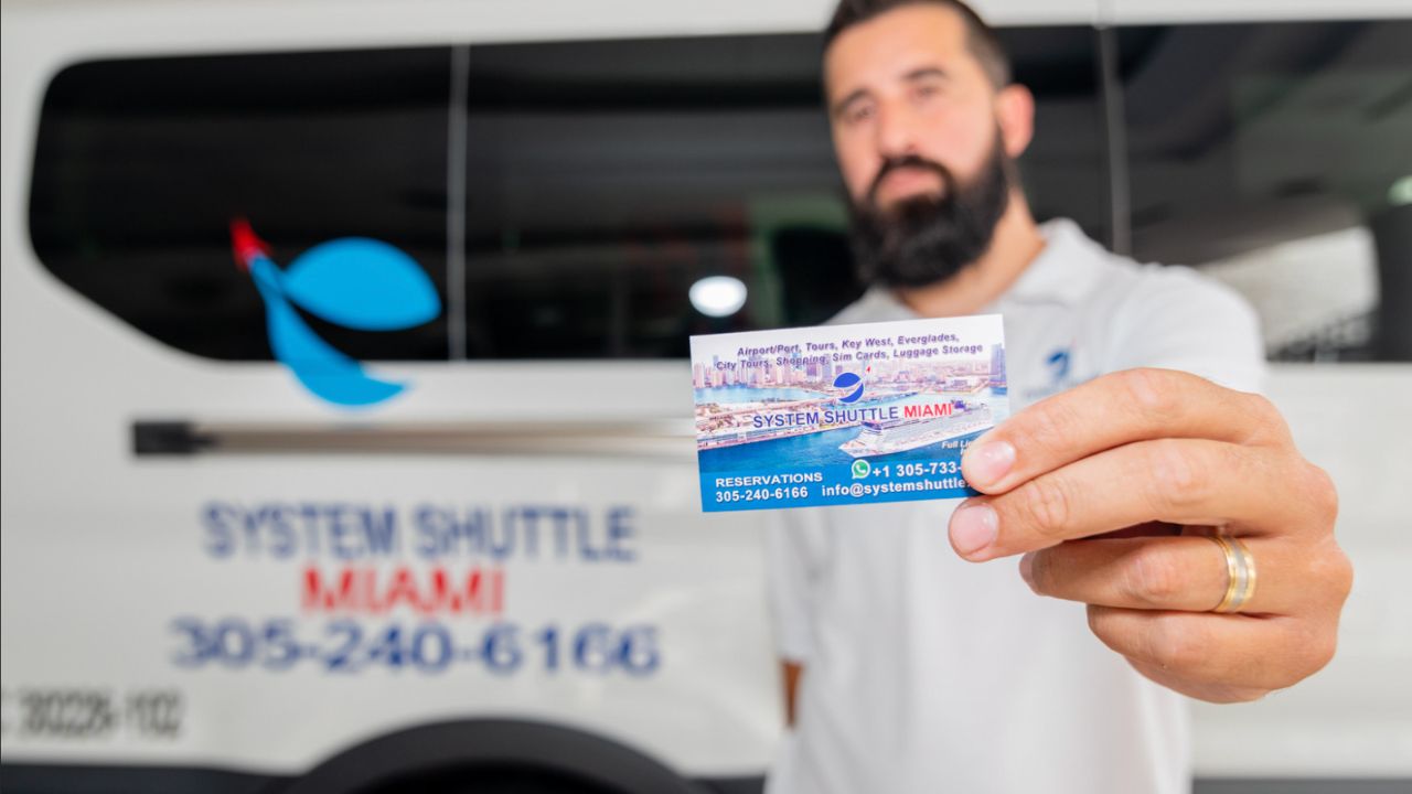 A member of System Shuttle Miami holding a business card in front of a branded shuttle van