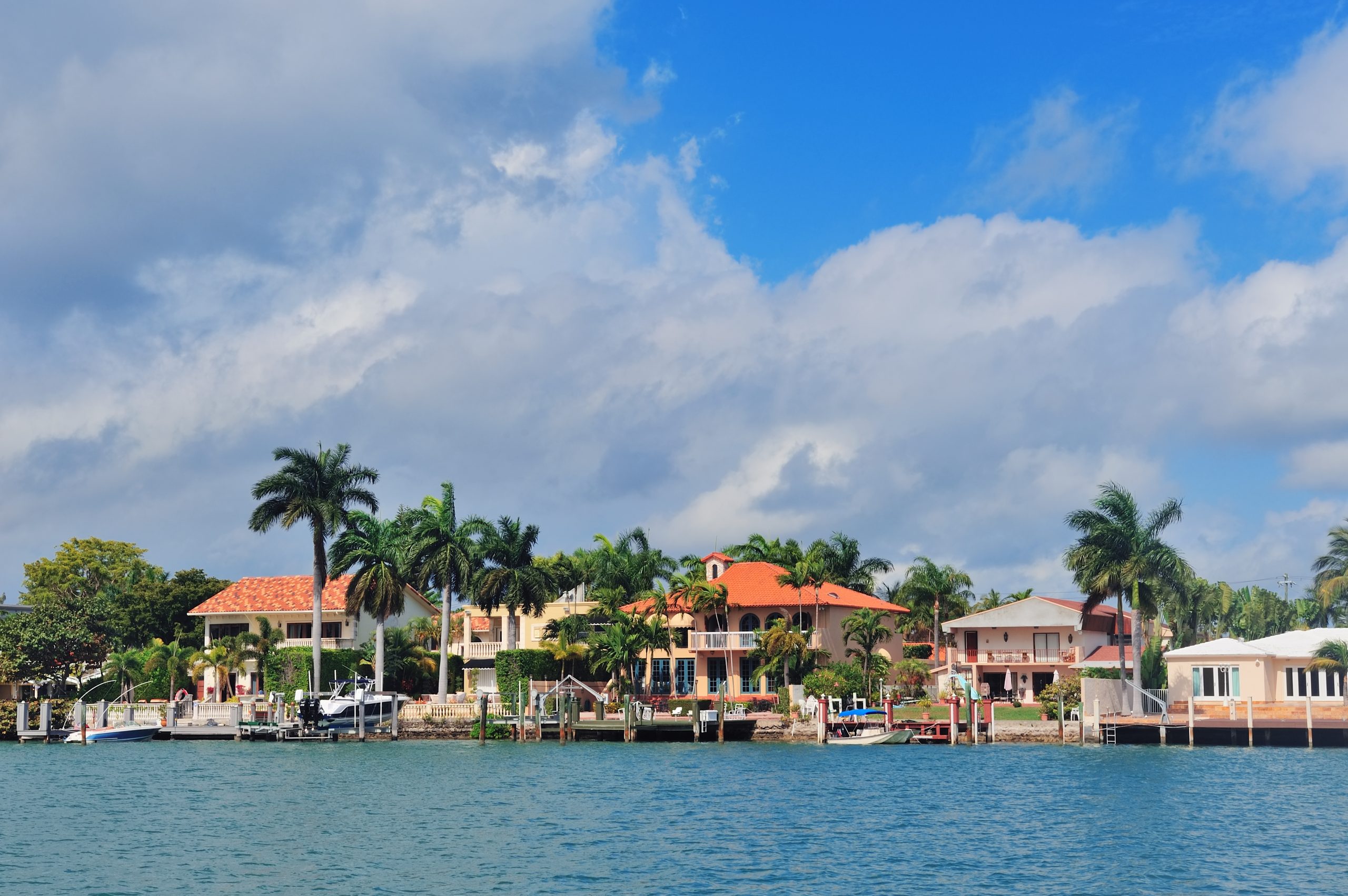 Waterfront Miami mansions with palm trees and private docks under blue sky at Biscayne Bay