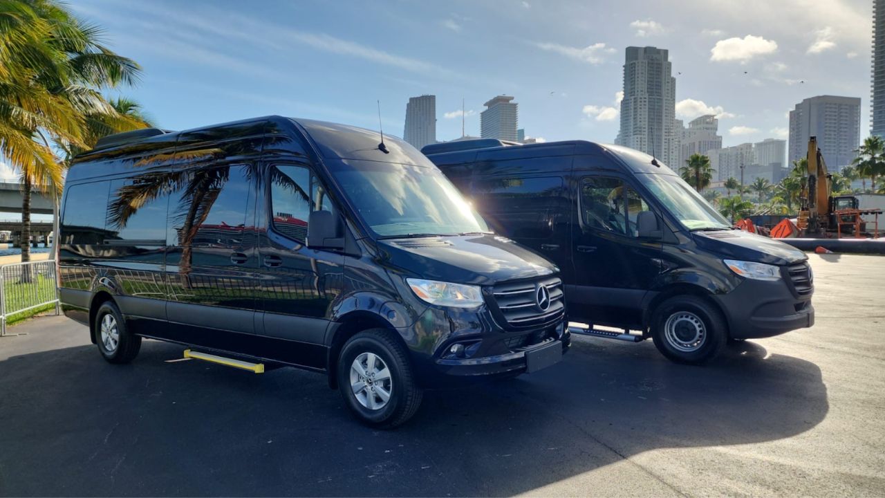 Two black shuttle vans by System Shuttle Miami parked with Miami skyline in the background