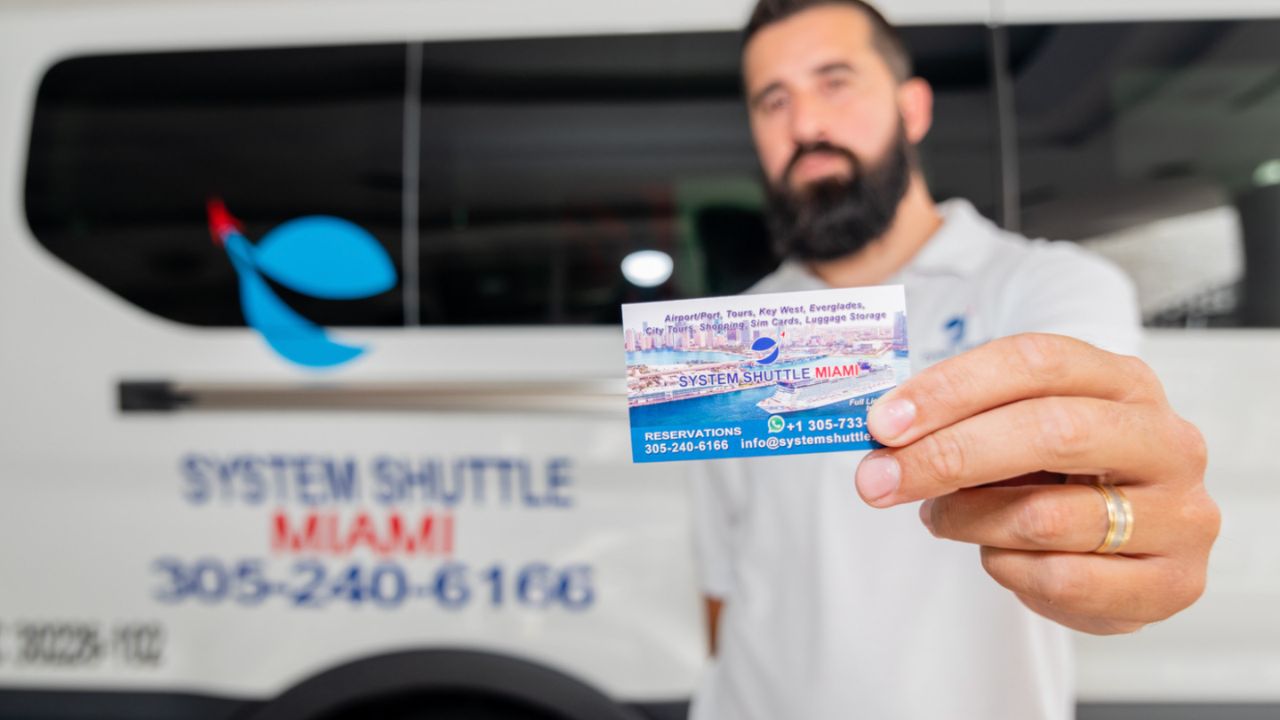 Crew member holding System Shuttle Miami business card in front of shuttle van