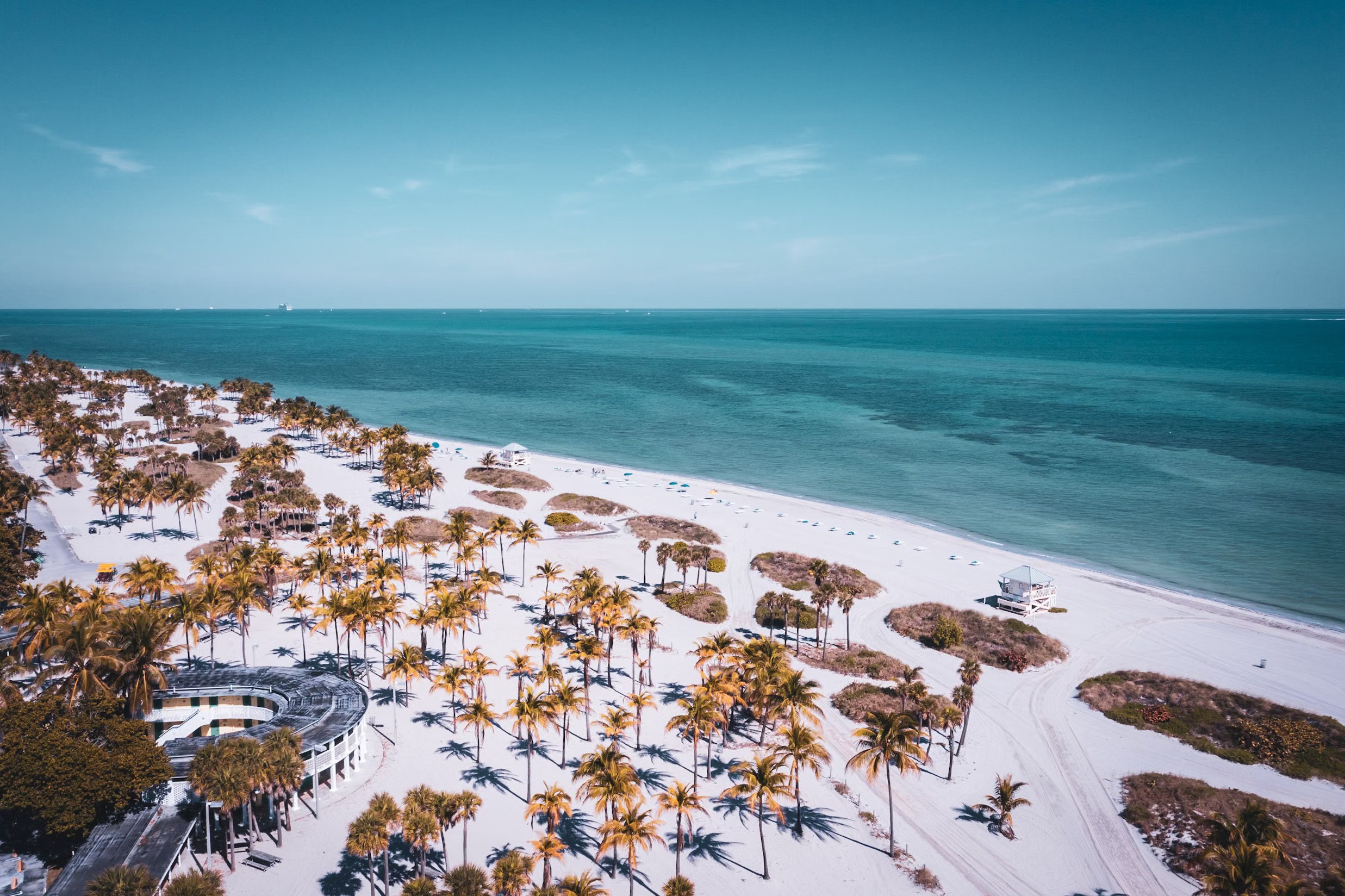 Aerial view of a beach with white sand, palm trees, and turquoise waters
