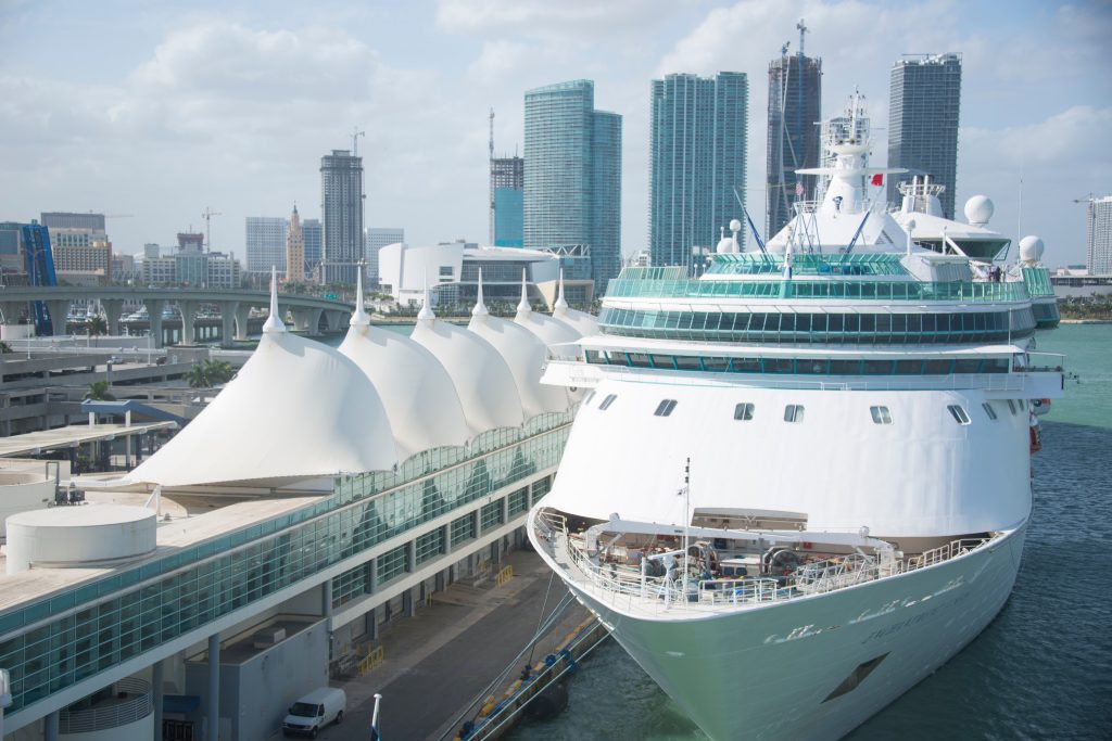 Large cruise ship docked at PortMiami cruise terminal with the Miami skyline in the background