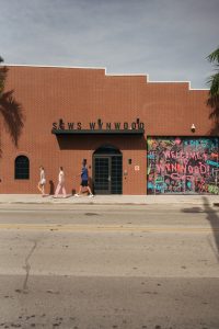 Visitors walking past the Welcome to Wynwood mural and colorful storefront in Miami's Wynwood Arts District