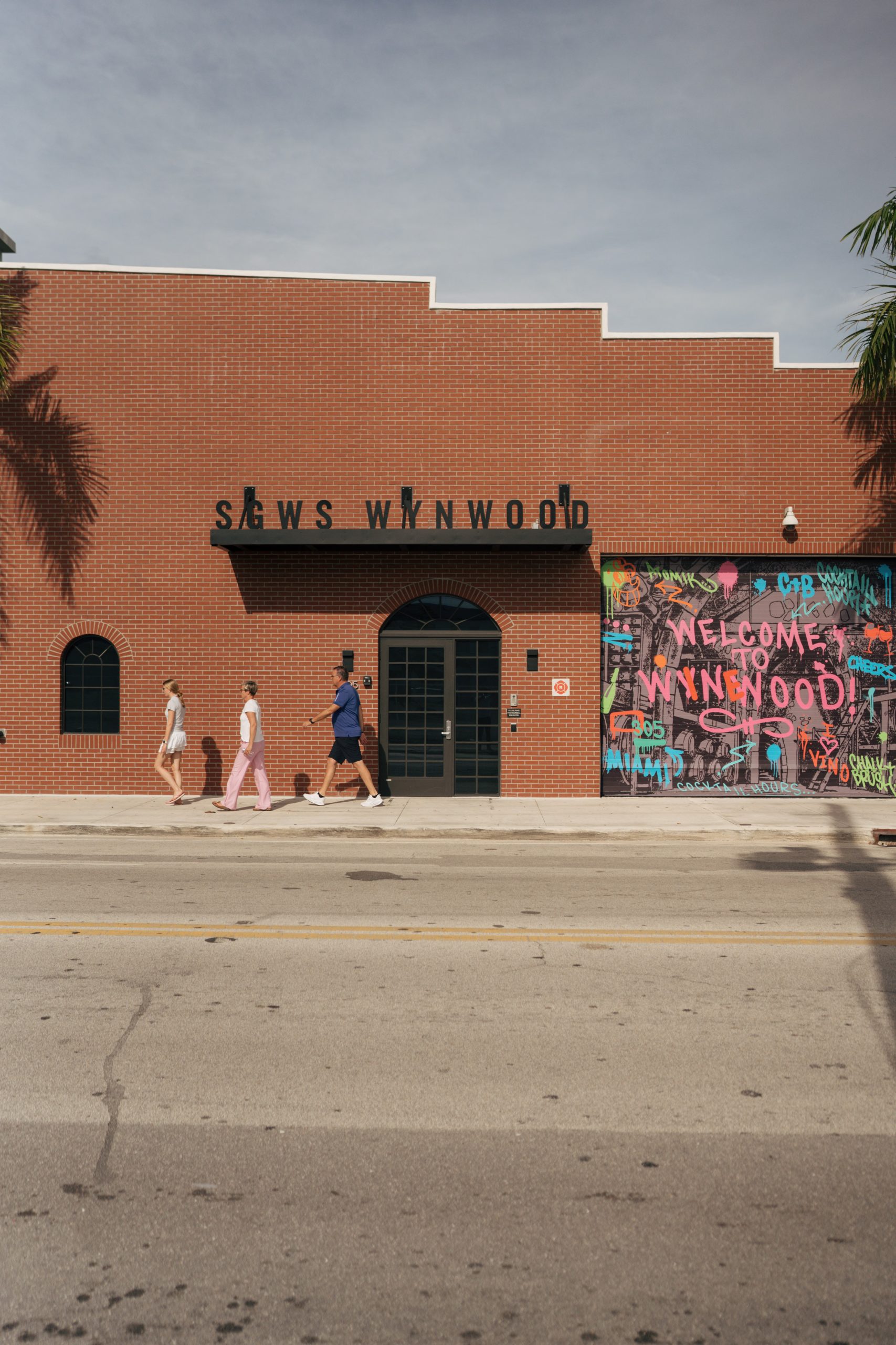 Visitors walking past the Welcome to Wynwood mural and colorful storefront in Miami's Wynwood Arts District