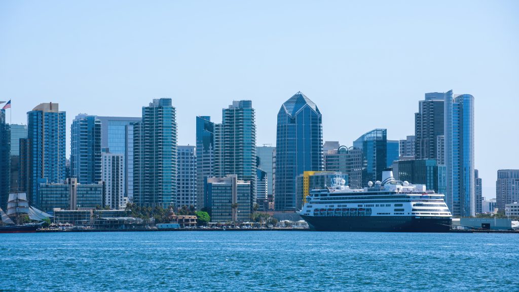 Cruise ship docked along the Miami waterfront with the downtown skyline in the background on a clear day.