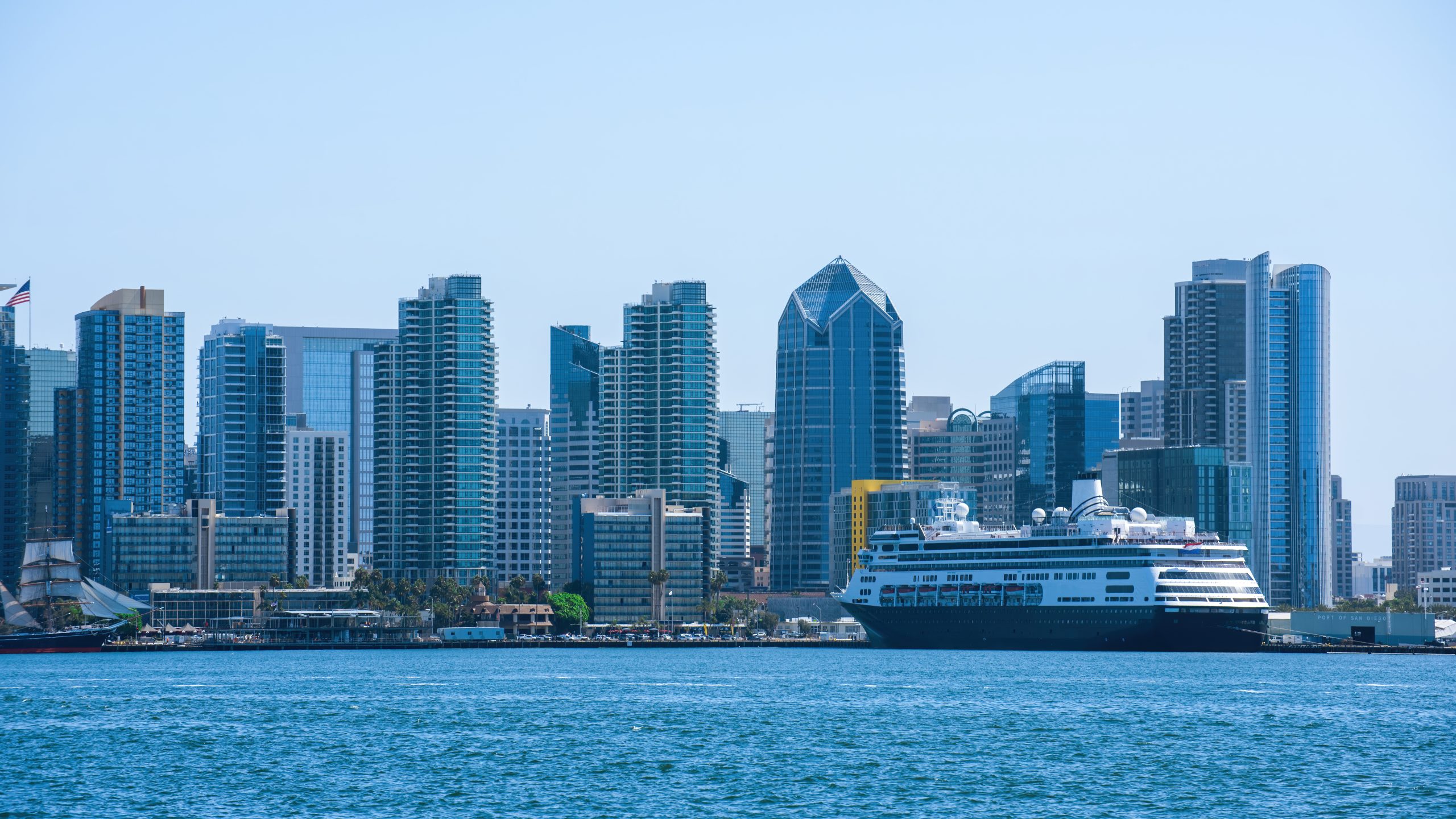 Cruise ship docked along the Miami waterfront with the downtown skyline in the background on a clear day.