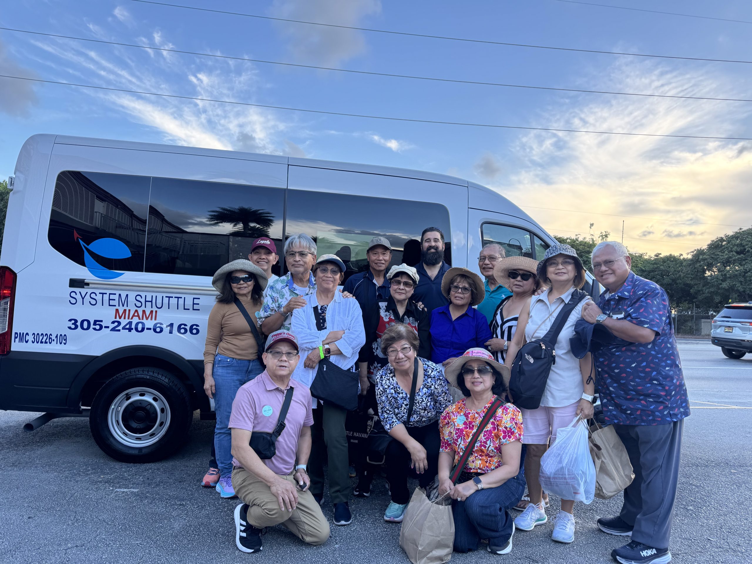 Happy group of travelers posing beside a System Shuttle Miami van before a sightseeing tour or airport transfer service.