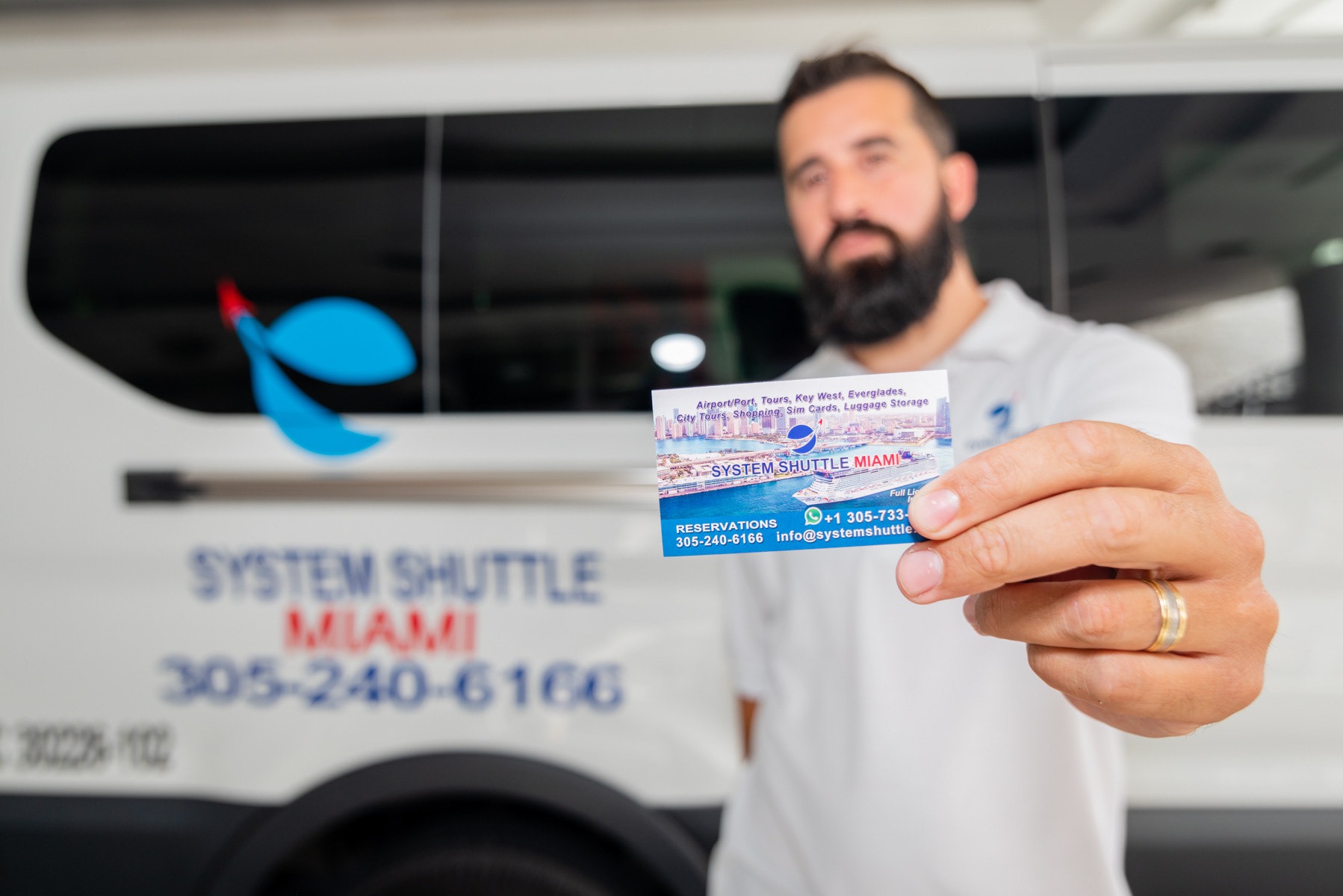 System Shuttle Miami representative holding a business card promoting airport transportation and sightseeing services.