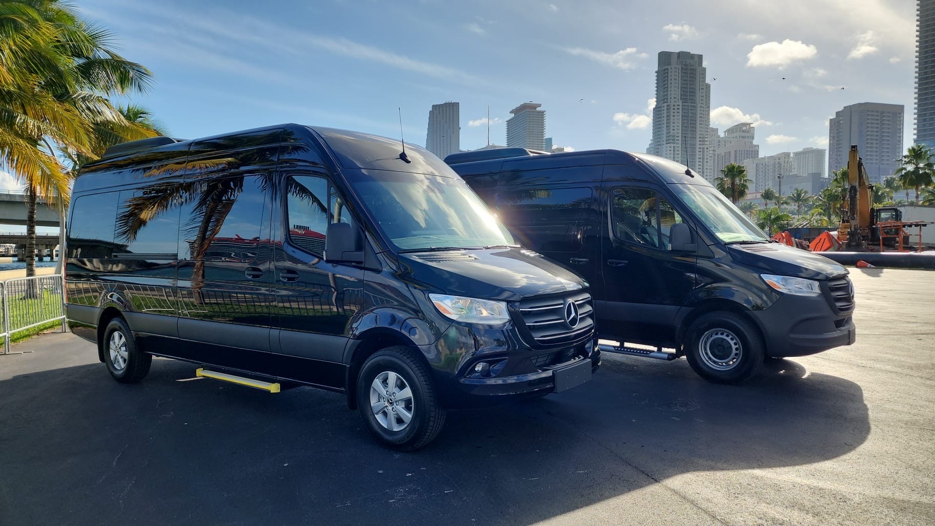 Black Mercedes Sprinter shuttle vans parked near palm trees and city skyscrapers.