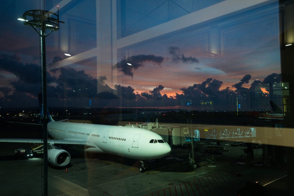 Passenger airplane parked at an airport gate at sunset, viewed through terminal windows